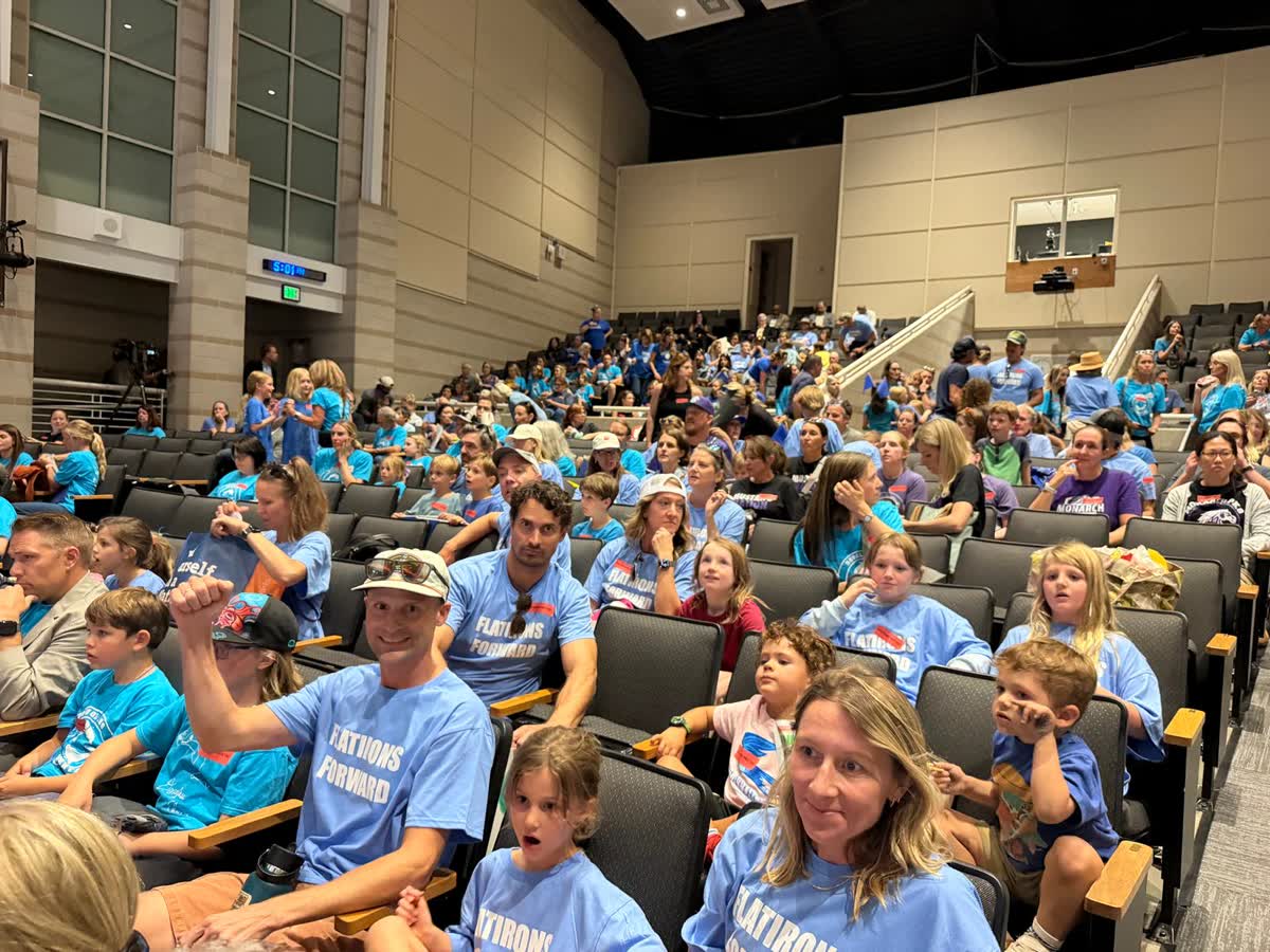 Un auditorio lleno de familias con camisetas escolares azules y verde azulado antes de la reunión de BVSD.