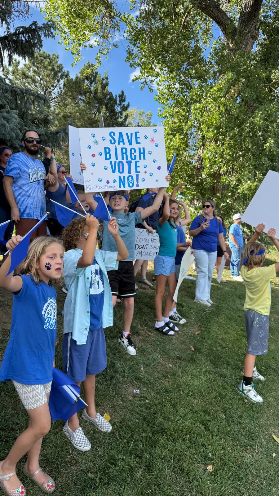 Niños con camisetas azules en el pasto sosteniendo un cartel hecho a mano que dice Save Birch, vote no.
